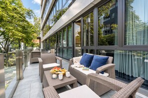 A modern outdoor seating area with wicker furniture, a glass partition, and a view of the cityscape.