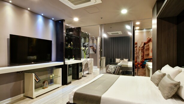 Ein modernes Hotelzimmer mit einem großen Bett, einem Flachbildfernseher, einem Glastisch und einer Sitzecke mit einer Couch und Sesseln.