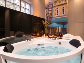 A spa room with a hot tub, a dining table with food and drinks, and a mural of a building.