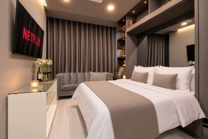 Un dormitorio moderno con una cama grande, un sofá, un televisor montado en la pared y una estantería.