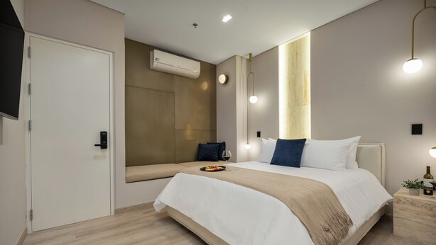 A modern hotel room with a large bed, bedside tables, a flat-screen TV, and an air conditioning unit.