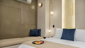 A hotel room with a bed, a bedside table with a plate of food and a glass of wine, and a wall-mounted air conditioner.