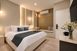 A modern hotel room with a large bed, bedside table, and a small seating area.