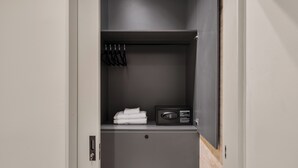 A walk-in closet with a dark gray door, a hanging rack with black hangers, a folded towel on the shelf, and a black safe.