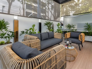 A modern outdoor seating area with a grey sofa, wicker chairs, and a glass table with drinks.