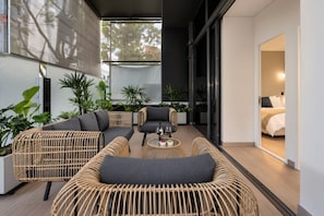 A modern outdoor seating area with wicker furniture and a glass door leading to a bedroom.