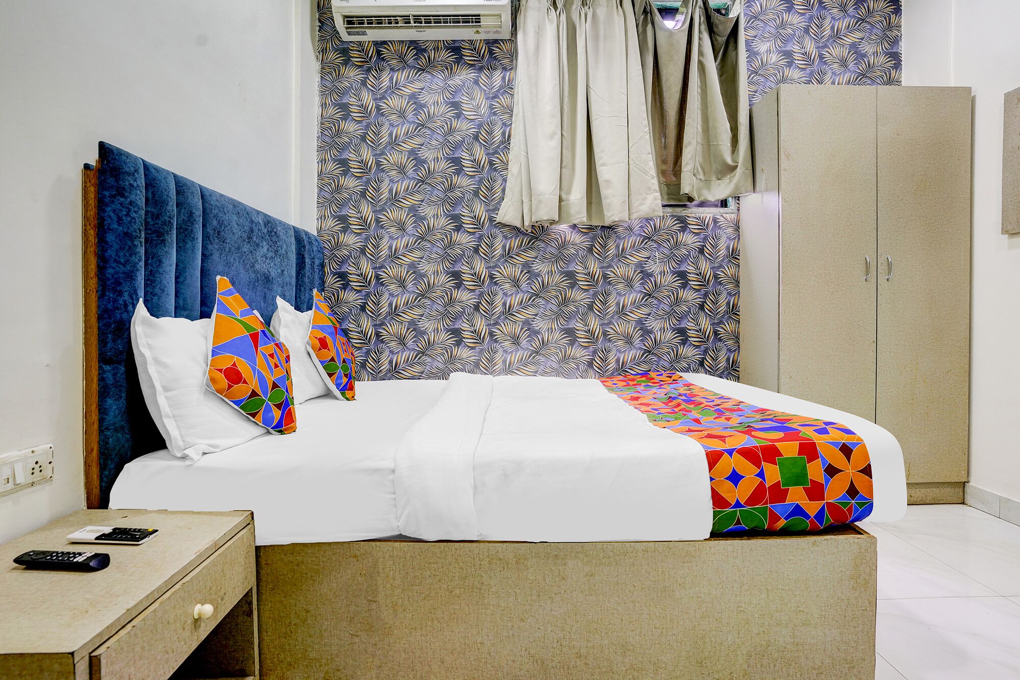 Ein Bett mit einer farbenfrohen Decke mit geometrischem Muster, einem Kopfteil und Kissen mit abstrakten Designs.