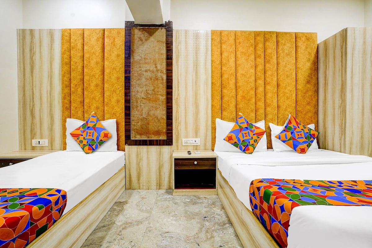 Habitación de hotel con dos camas, cabecero de madera, mesita de noche pequeña con teléfono y una lámpara de pared.