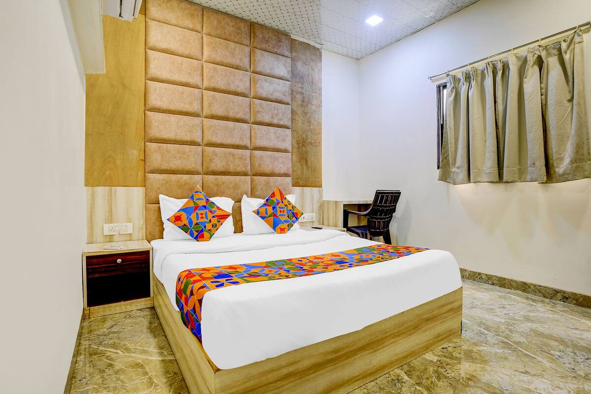 Habitación de hotel con una cama grande, cabecero, mesita de noche, una silla y una ventana con cortinas.