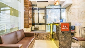A lobby with a brown leather sofa, a reception desk with a 'fab express' sign, and a glass door leading to a hallway. - Fabexpress Konak (Mumbai)