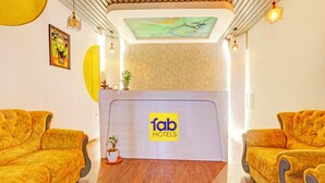 Un área de recepción con un letrero de 'fab hotels', dos sofás amarillos acolchados, una pequeña planta en maceta y suelo de madera.
