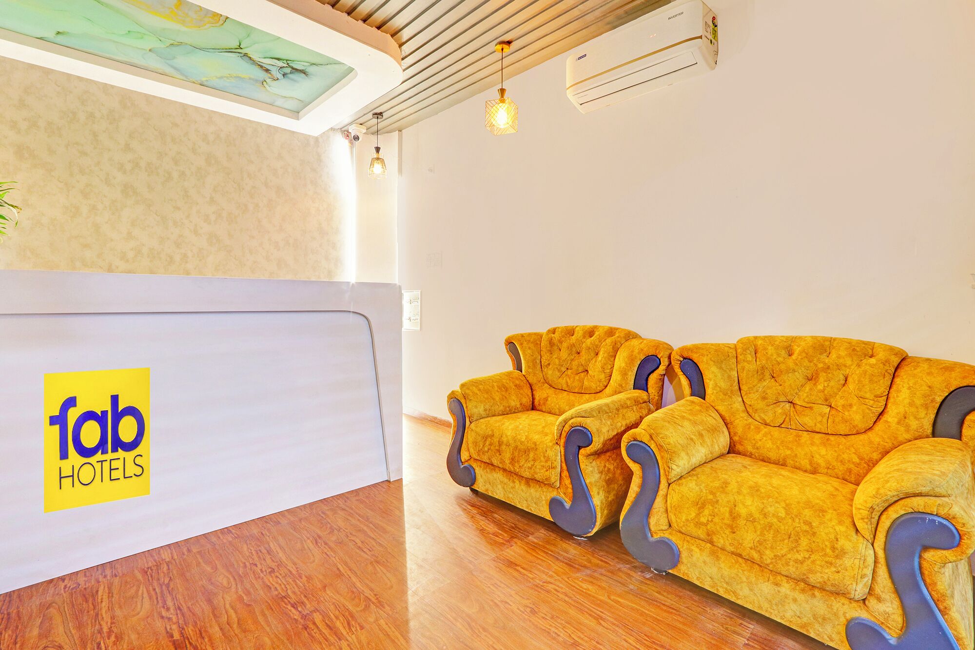 A reception area with a reception desk labeled 'tab hotels', a yellow sofa, wooden flooring, and a ceiling with a light fixture and air conditioning unit.