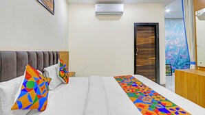 Habitación de hotel con cama, almohadas, cómoda, espejo, unidad de aire acondicionado y puerta.