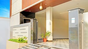 Una entrada de edificio moderno con un sendero adoquinado que lleva a una puerta, una planta en maceta y una lámpara colgante.