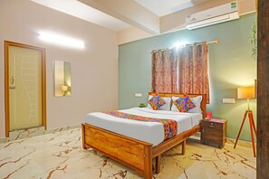 A hotel room with a wooden bed, a nightstand, a lamp, and a wall-mounted air conditioner. - FabHotel Kings Palace Manyata - Near Manyata Tech Park Main Gate (Bangalore)