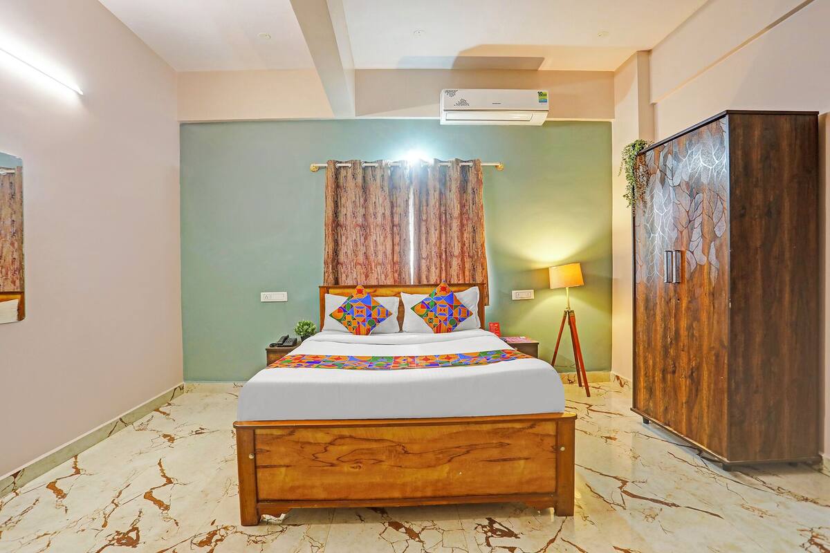 A bedroom with a wooden bed, a nightstand, a lamp, an air conditioning unit, and a wardrobe.