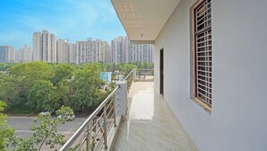 A balcony with a view of high-rise buildings and greenery. - Fabhotel Mvr Stay 116 (Noida)