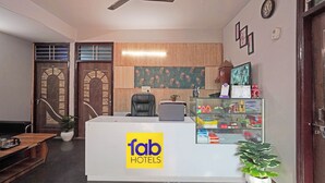 A reception desk with a logo for 'fab hotels', a black office chair, a computer, a shelf with various items, a clock, and a decorative wall panel. - Fabhotel Mvr Stay 116 (Noida)