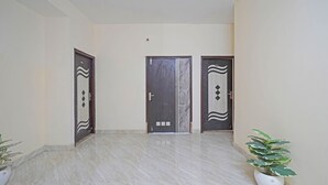 A hallway with three doors, each with a unique design, leading to different rooms. The floor is tiled, and there are potted plants on either side. - Fabhotel Mvr Stay 116 (Noida)