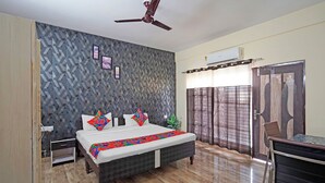 A bedroom with a bed, a ceiling fan, an air conditioning unit, a window with curtains, and a wooden door. - Fabhotel Mvr Stay 116 (Noida)