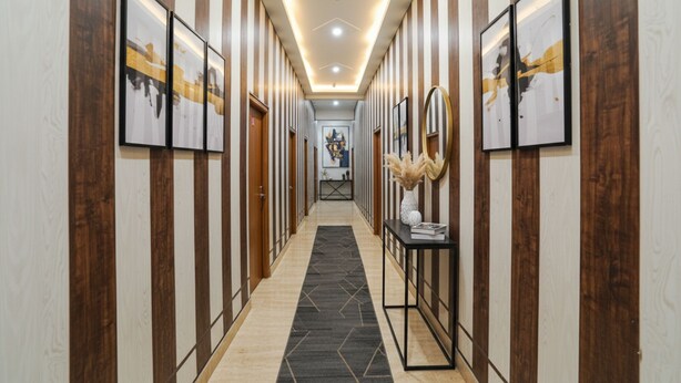 A hallway with striped walls, framed artwork, a vase with dried plants, and a table with a book. - Fabhotel Rk Dham (Vrindavan)