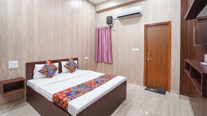 A bedroom with a wooden bed, a bedside table, a wardrobe, an air conditioning unit, and a door. - Fabhotel Rk Dham (Vrindavan)