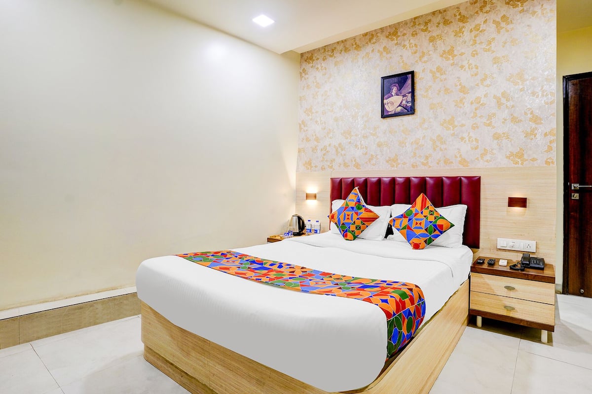 A hotel room with a large bed, a wooden nightstand, a red upholstered headboard, and a wall-mounted picture.