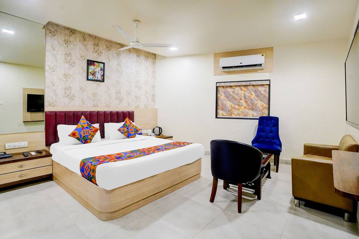 A hotel room with a bed, a desk, a chair, an air conditioning unit, and a ceiling fan.