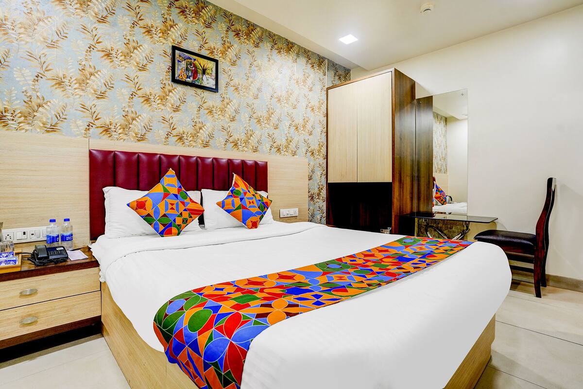A hotel room with a large bed, a wooden headboard, a desk with a chair, a mirror, and a patterned wallpaper.