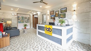 A hotel reception area with a modern design, including a reception desk, seating area, and a ceiling fan. - FabHotel Golden Grand Inn - Global Village (Bangalore)