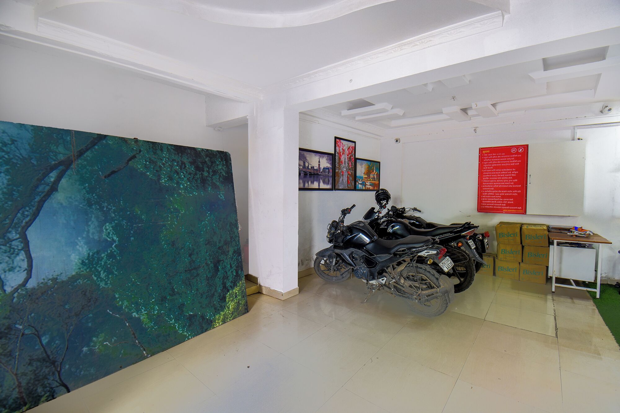 A room with a motorcycle, a large abstract painting, and several framed pictures on the wall.