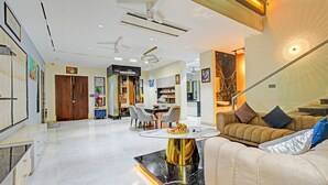 Un salon moderne avec une table basse en marbre, un canapé avec des coussins, un coin repas avec des chaises et une cuisine en arrière-plan.