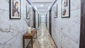 A hallway with marble walls, framed artwork, a wooden bench with a vase and books, and a marble floor. - FabHotel Golden Comforts (Bengaluru)