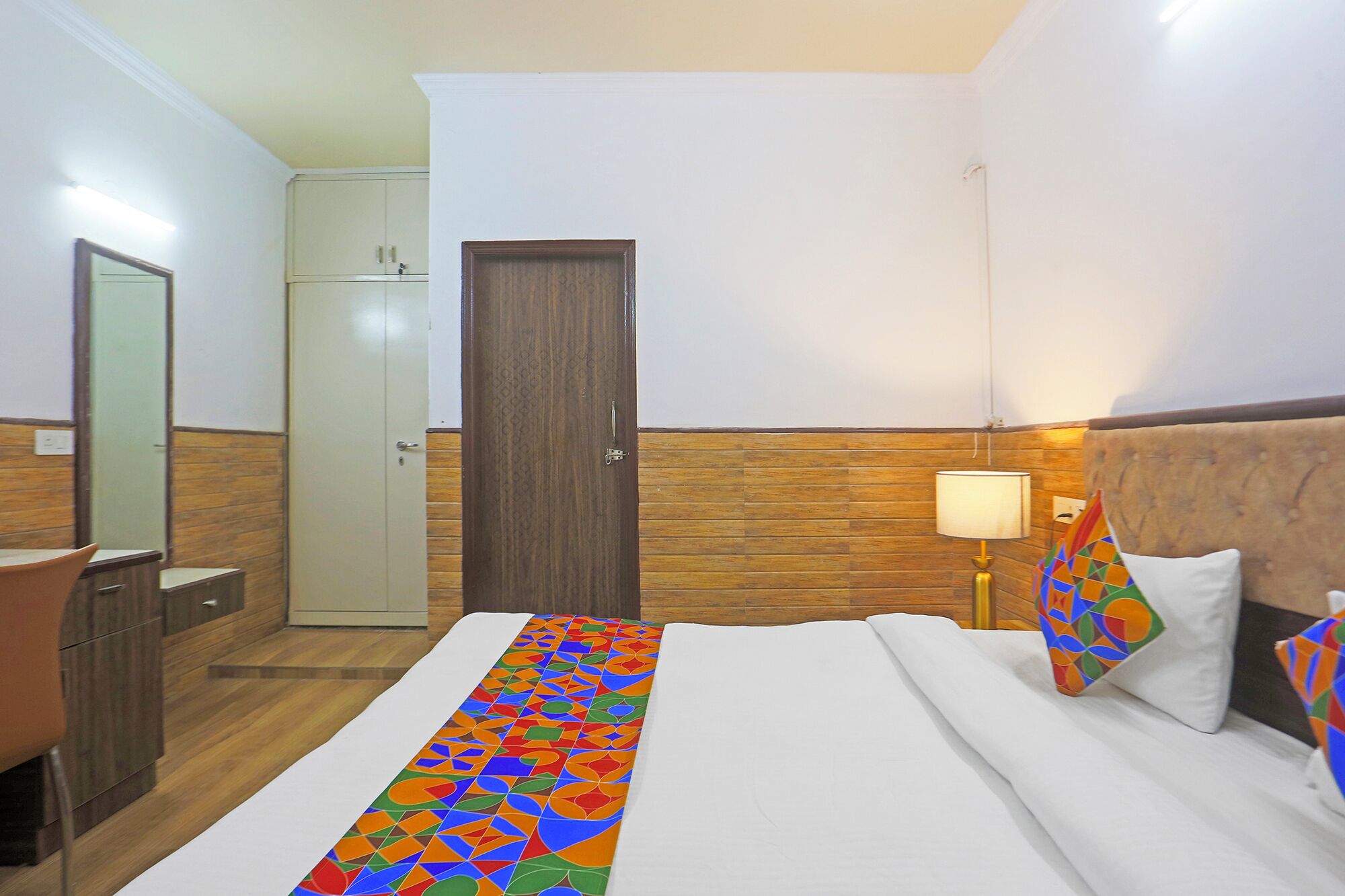 A hotel room with a bed, a bedside table, a lamp, a wardrobe, and a door.