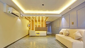 A hotel reception area with a reception desk, a sofa, and a wooden panel wall. - FabHotel Baba's Inn (New Delhi)