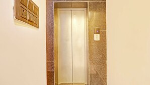 An elevator with a control panel on the wall, a door, and a wall-mounted light switch. - FabHotel Baba's Inn (New Delhi)