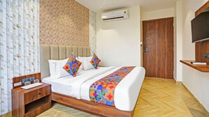 A hotel room with a bed, a wooden nightstand, an air conditioning unit, a television, and a wooden door. - FabHotel Baba's Inn (New Delhi)
