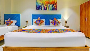 A hotel room with two beds, each with a blue headboard and colorful geometric pillows. A large painting of a waterfall hangs above the beds. - FabHotel Siddharth Inn - Nr. Siddharth Bunglows (Gandhinagar)