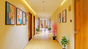 A hotel hallway with wooden doors, framed artwork on the walls, and potted plants. - FabHotel Siddharth Inn - Nr. Siddharth Bunglows (Gandhinagar)