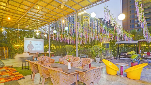 An outdoor seating area with a covered patio, a grill, and hanging plants. - FabHotel Siddharth Inn - Nr. Siddharth Bunglows (Gandhinagar)