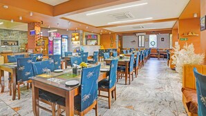 A restaurant with multiple dining tables and chairs, a kitchen area, and a ceiling fan. - FabHotel Siddharth Inn - Nr. Siddharth Bunglows (Gandhinagar)