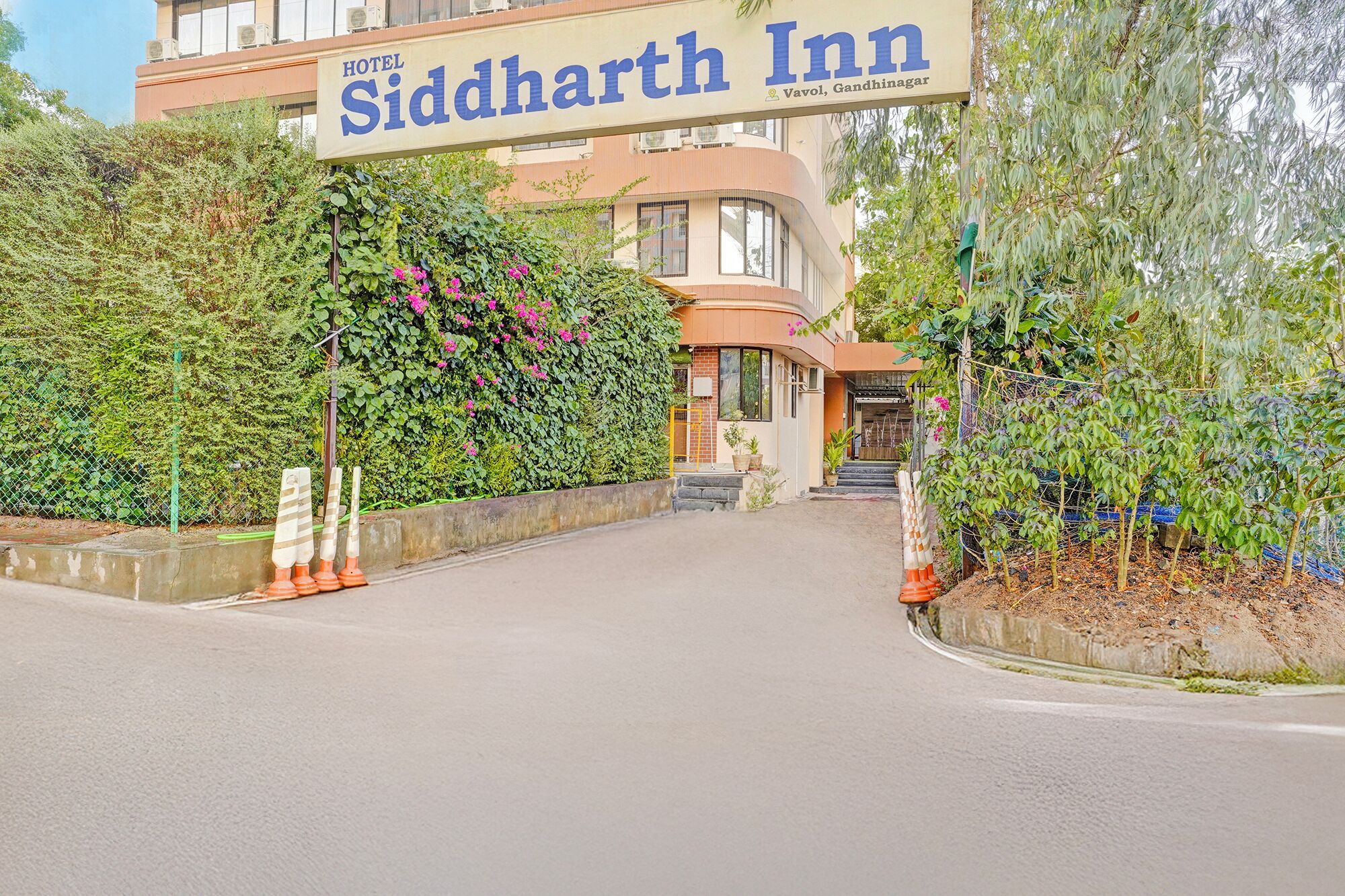 De ingang van Siddharth Inn, met een opvallend bord, een gebogen gevel en weelderige begroeiing.