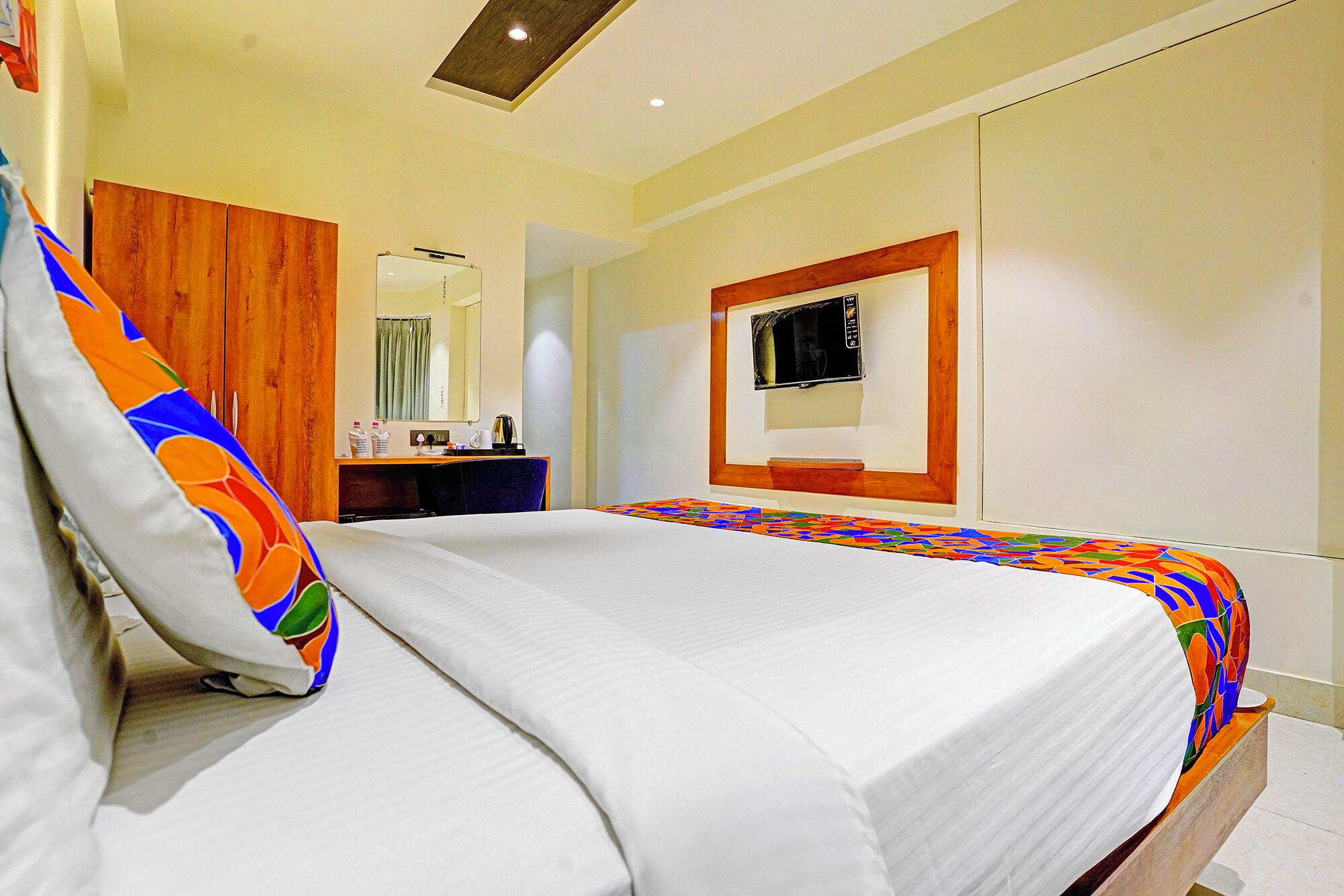 A hotel room with a bed, a desk, a mirror, and a television.