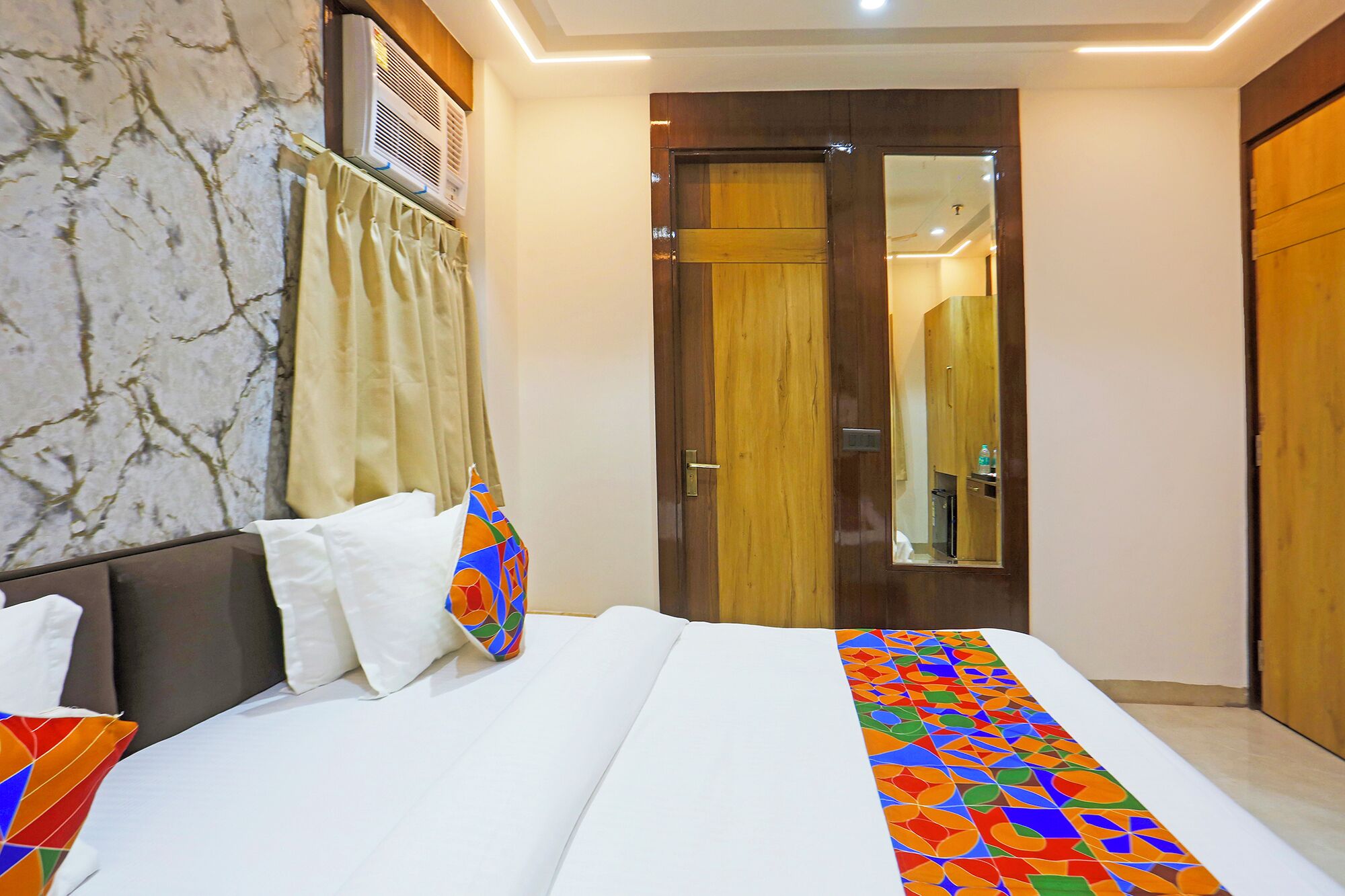 A hotel room with a bed, a mirror, a wardrobe, and a door.