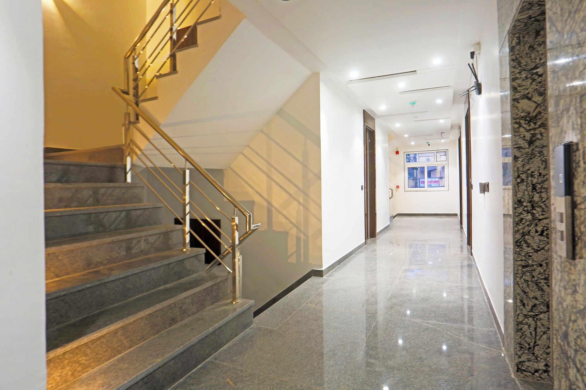 A modern hotel corridor with marble flooring, a staircase with metal railings, and a clean, well-lit environment.