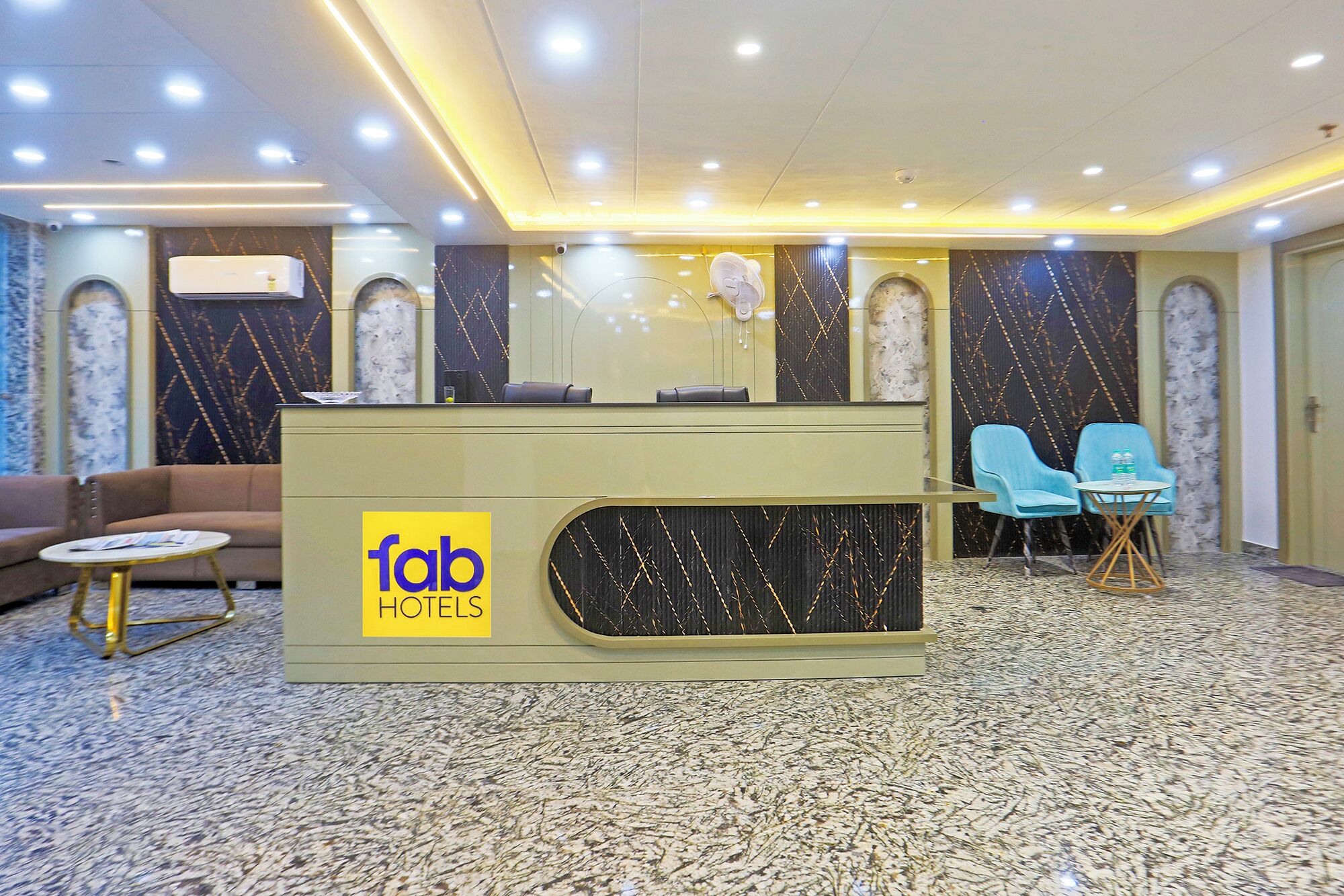 A hotel reception area with a reception desk, a sofa, two chairs, and a small table.