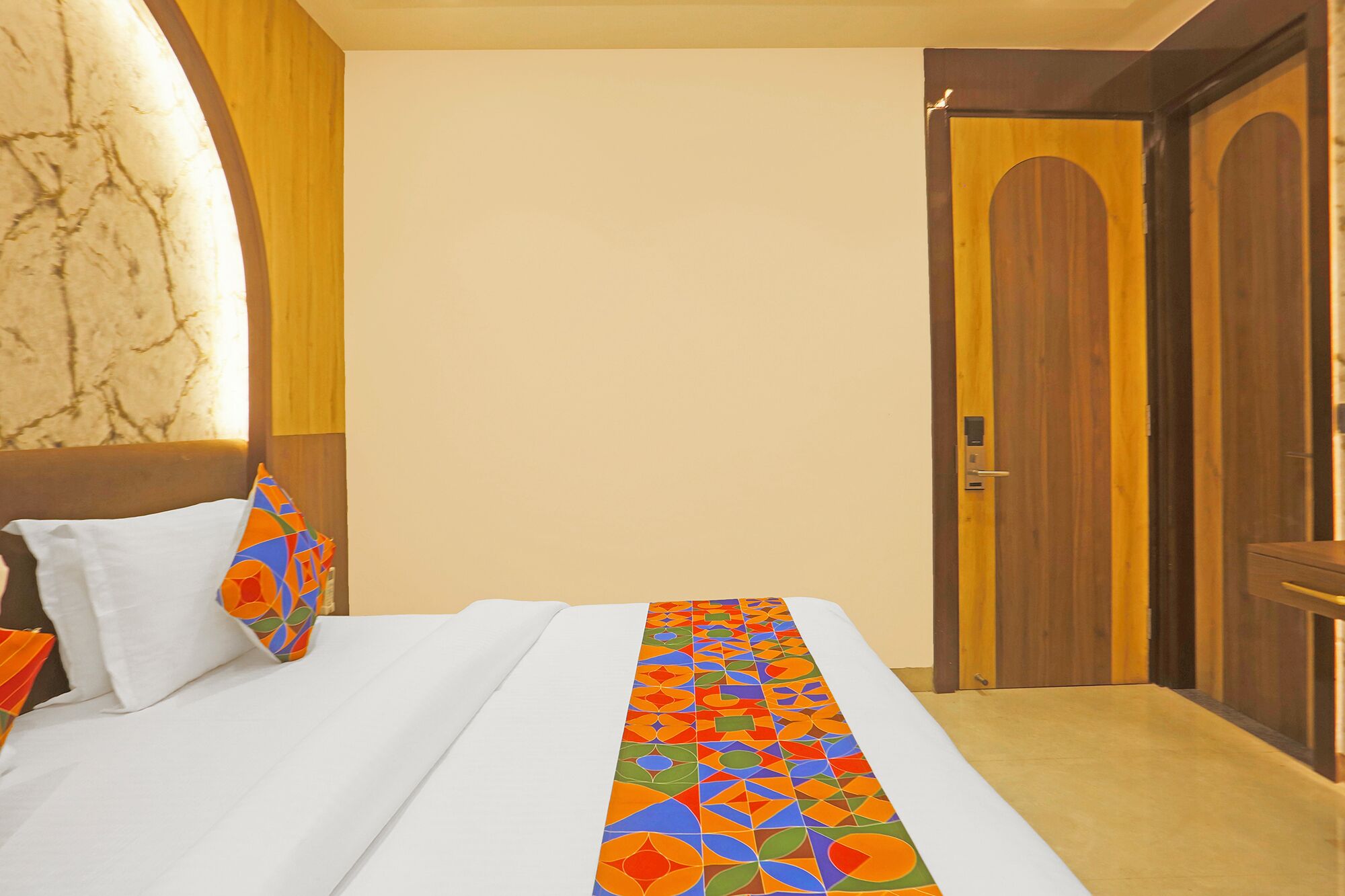 A hotel room with a bed, a patterned bed runner, a wooden door, and a marble wall.