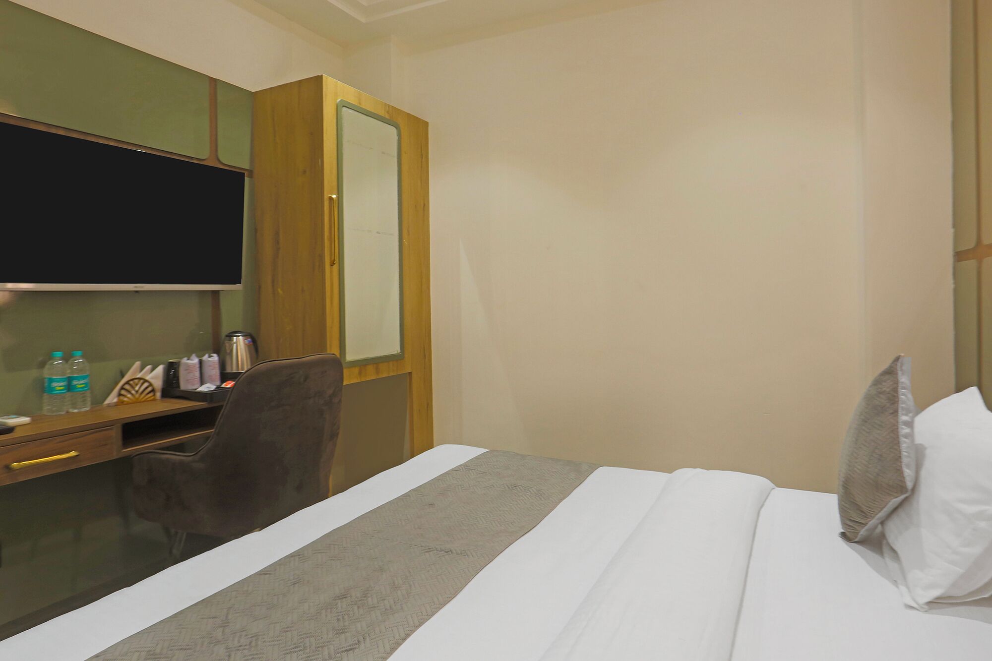 Habitación de hotel con cama, escritorio con silla, espejo y mesita con tetera y tazas.