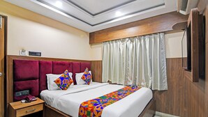A hotel room with a wooden headboard, a bed with white linens, a colorful geometric throw blanket, a bedside table with a telephone, and a window with white curtains. - Fabhotel The Crystal (Kolkata)
