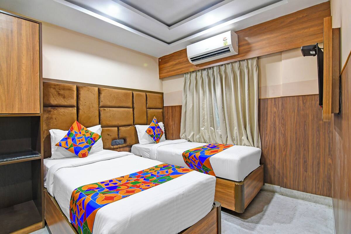 A hotel room with two beds, a wooden headboard, an air conditioning unit, and a curtain.
